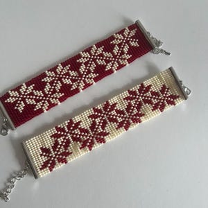 Puede incluir: Dos pulseras de cuentas con un patr&oacute;n de copo de nieve. Una pulsera es roja con copos de nieve blancos, y la otra es blanca con copos de nieve rojos.