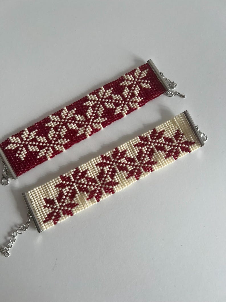 Puede incluir: Dos pulseras de cuentas con un patr&oacute;n de copo de nieve. Una pulsera es roja con copos de nieve blancos, y la otra es blanca con copos de nieve rojos.