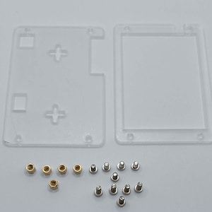 以下が含まれることがあります： 丸みを帯びた角とネジ穴のある透明なプラスチック製の長方形のケースが2つ。ケースは空で、小さな銀色のネジと金色のナットのセットが付属しています。
