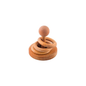 May include: Wooden stacking toy with a round base, a central post, and three rings. A wooden ball sits atop the post. The toy is made of light-colored wood and is designed for young children.