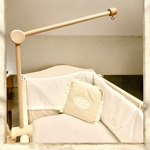 Op de afbeelding: Een houten babymobielarm met een wit en beige babybeddengoedset. Het babybeddengoed heeft een decoratief kussen met de tekst "De kleine prins" erop.