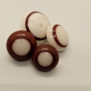 May include: Four round buttons with a white centre and a brown outer ring. The buttons have a single brown stripe around the centre.