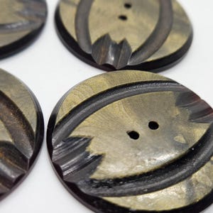 Puede incluir: Cuatro botones redondos de dos agujeros con un diseño marmoleado en negro y dorado. Los botones tienen un patrón texturizado en relieve.