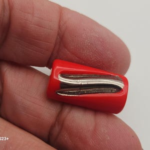 May include: A small, red, rectangular object with two silver-colored, curved metal pieces. The object is held in a hand, and the background is a light color.