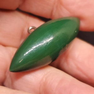 May include: A dark green, teardrop-shaped pendant with a small silver loop at the top. The pendant has a smooth, glossy finish and a pointed end. The object is held in a person's hand.