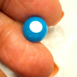 Puede incluir: Primer plano de una cuenta de vidrio azul y blanco. La cuenta es redonda y tiene un centro blanco.