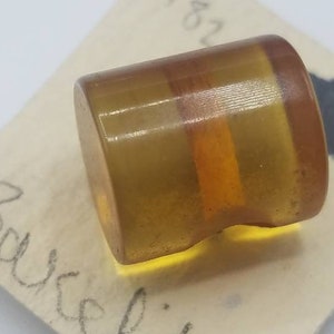 Può includere: Un bottone rotondo di colore ambrato con un design a strati. Il bottone ha una finitura liscia e lucida.