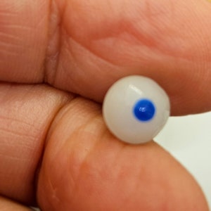 Puede incluir: Un ojo de vidrio blanco con un iris azul. El ojo tiene un diámetro de aproximadamente 2,5 cm.