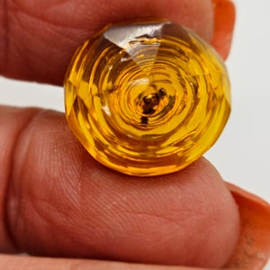 May include: A close-up of a faceted, round, amber-coloured glass object. The object has a spiral design in the centre and is held between two fingers. The glass reflects light, creating a sparkling effect.