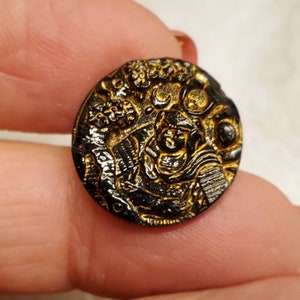 May include: A black glass button with a gold-coloured design. The design features a floral pattern and a crescent moon.