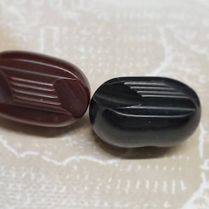 May include: Two oval-shaped buttons, one dark brown and one black, with a decorative grooved pattern.