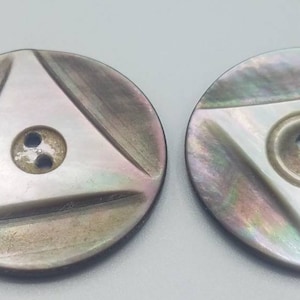 May include: Two iridescent mother-of-pearl buttons with a triangular design and two holes. The buttons are a light grey colour with a subtle shimmer.