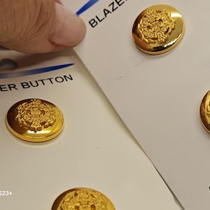 Botones antiguos - 4 medianos, 2 tarjetas de 1/2", 13 mm. Nuevos, de plástico metalizado bronce en cartulina, diseño de escudo, marca JHB (21-25 de enero).