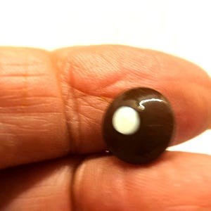 Puede incluir: Una piedra preciosa cabujón ovalada de color marrón oscuro con un centro blanco.