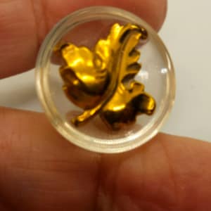 May include: A clear glass button with a gold leaf design.