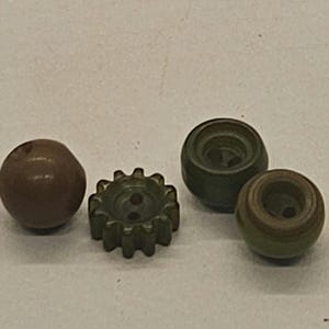 May include: Four small, vintage-style wooden components in shades of brown and green. The items include a round bead, a cog-shaped piece, and two small, rounded cylinders. These components could be used for crafts or jewelry making.
