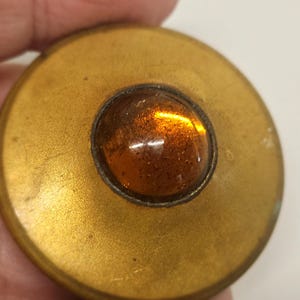 May include: A gold-toned button with a round, amber-colored glass center.