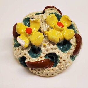 May include: A ceramic sculpture of a coral reef with two yellow flowers with red centers. The coral is white with brown and green accents.