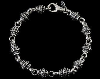 May include: A silver bracelet with a series of cylindrical beads, each adorned with small, raised dots. The beads are connected by small, rounded links. The bracelet has a lobster clasp closure. The jewelry is displayed against a black background.