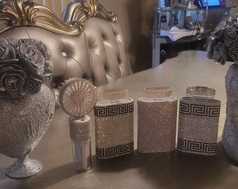May include: A set of six silver and black decorative containers with a geometric pattern. The containers are arranged on a table with a silver heart-shaped vase and a silver vase with a floral arrangement.