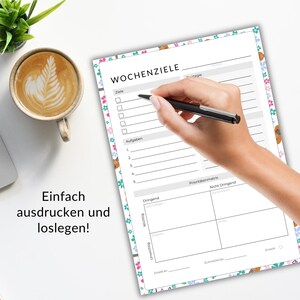 May include: A weekly planner with floral border is being filled out with a pen. The planner has sections for goals, tasks, and a priority matrix. Text on the planner reads "WOCHENZIELE". A cup of coffee sits nearby.
