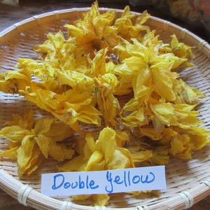 May include: Dried yellow flower petals in a woven basket. The petals are arranged in a loose pile and have a delicate, papery texture. A blue label with the text "Double Yellow" is placed in front of the petals.