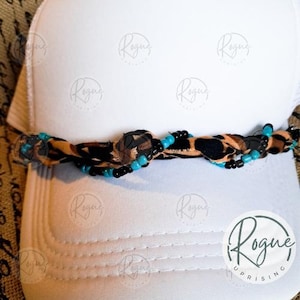 May include: White trucker hat with a decorative band featuring a leopard print pattern, black beads, and turquoise beads. The hat has a curved brim and a mesh back. The band is knotted in the center.