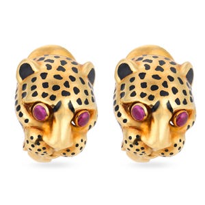May include: A pair of gold hoop earrings shaped like leopard heads, featuring black enamel spots and round, vibrant pink gemstone eyes. The earrings have a polished metallic finish and a detailed, three-dimensional feline facial structure.