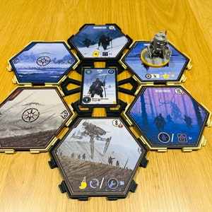 May include: A hexagonal game board with six tiles, each featuring a different landscape scene. The tiles are arranged in a circular pattern, with a central space for a card. The tiles are made of cardboard and have a gold border. The card in the center is a character card from the game "Star Wars: Destiny".