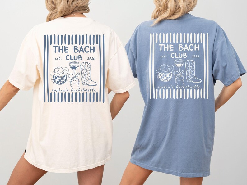 May include: Two oversized t-shirts, one cream and one blue, feature a graphic on the back with the text "THE BACH CLUB est. 2026" and illustrations of a cowboy hat, cocktail, and boot. The shirts are for a bachelorette party.