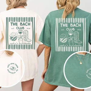 May include: Two oversized t-shirts, one cream and one green, featuring a white graphic design. The design includes the text "THE BACH CLUB est. 2026" and illustrations of a cowboy hat, wine glass, and boots. The shirts also have a small circular graphic that says "WITH LOVE FROM NASHVILLE, TN."