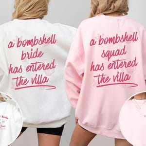 May include: A white sweatshirt with pink text reading 'a bombshell bride has entered the villa' and a pink sweatshirt with text reading 'a bombshell squad has entered the villa', both featuring small shell graphics and front chest logos.
