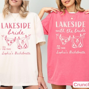May include: An ivory t-shirt and a crunchberry pink t-shirt, each featuring a graphic of two bikinis hanging on a clothesline. The text reads LAKESIDE bride or LAKESIDE with the bride, 2026 LAKE TAHOE, and Sophia's Bachelorette in pink lettering.