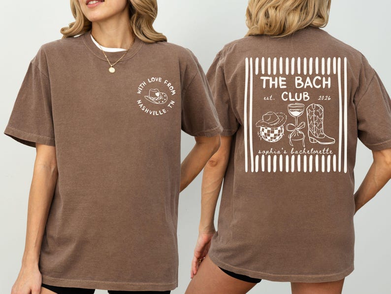 May include: Brown t-shirt with white text and graphics. Front reads "WITH LOVE FROM NASHVILLE, TN" in a circle. Back features "THE BACH CLUB est. 2026" with a cowboy hat, disco ball, wine glass, and boot.