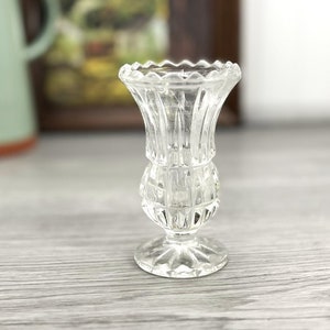 May include: A clear glass vase with a cut glass design. The vase has a wide mouth and a narrow base.