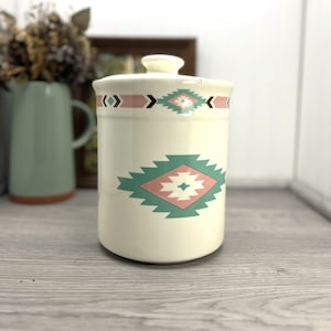 May include: White ceramic canister with a lid, featuring a Southwestern-inspired design with pink and green geometric patterns.