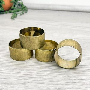 May include: Four gold-toned metal napkin rings. The rings are round and have a textured surface.