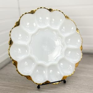 Pode incluir: Prato para ovos de vidro branco leitoso com borda dourada e borda festonada. O prato tem 12 compartimentos individuais para servir ovos.