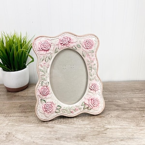 Puede incluir: Marco de fotos ovalado decorativo con borde festoneado. Pintado en rosa suave, presenta detalles en relieve de rosas rosas y hojas verdes. Diseñado para una foto.