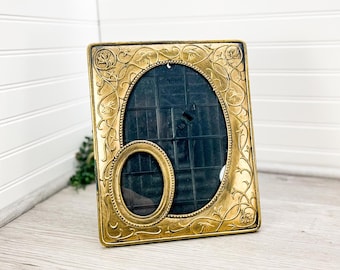 May include: A gold-toned picture frame with an ornate design featuring a floral motif. The frame has two openings for photos, one larger than the other.