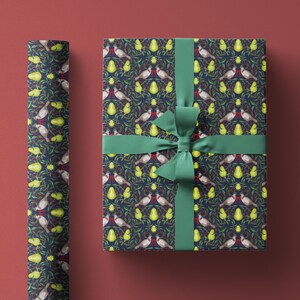 May include: Gift wrapped in patterned paper with a dark blue background, featuring birds, pears, and foliage. A green ribbon and bow secure the package. A roll of matching wrapping paper is visible on the left.