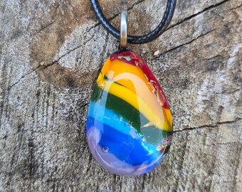 May include: A rainbow glass pendant on a black cord necklace. The pendant is teardrop shaped and has a swirl of colors including red, orange, yellow, green, blue, and purple.