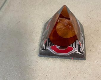 May include: A clear glass pyramid with a red, white, and black Ohio State University logo on the base. The pyramid is filled with a brown liquid.