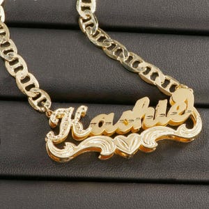 Può includere: Collana con catena dorata e ciondolo personalizzato a forma di placca con il nome "Kashia" in corsivo.