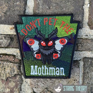 Op de afbeelding: Geborduurde patch met een zwarte Mothman met rode ogen en vleugels, tegen een groene en blauwe achtergrond. De patch leest "DON'T PET THE" erboven en "Mothman" eronder in witte tekst. De patch heeft de vorm van de staat Pennsylvania.