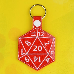 May include: Red felt keychain shaped like a twenty-sided die with white numbers 1 through 20. The keychain has a silver ring.
