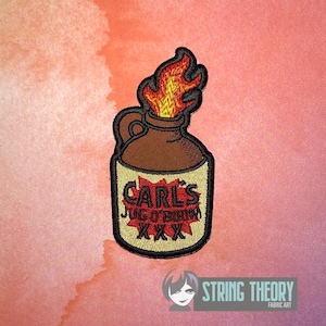 May include: An embroidered patch featuring a brown jug with a handle, topped with bright yellow and orange flames. The cream-colored label on the jug displays the black text "CARL'S JUG O' BOOM" over a red starburst shape, with "XXX" below.