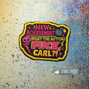 May include: A rectangular embroidered patch with a black background and a yellow border. It features pink and yellow text reading NEW ACHIEVEMENT WHAT THE ACTUAL FUCK, CARL?!, a pink skull, a pink lightning bolt, and a small grey bomb icon.