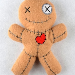 May include: A brown voodoo doll with a red heart, stitched seams, and an embroidered X for an eye.