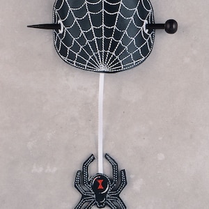 May include: Black spider web hair clip with a black spider hanging from it. The hair clip is made of leather and has a white string attached to it. The spider has a red hourglass on its back. The hair clip is a great way to add a touch of Halloween fun to your hair.